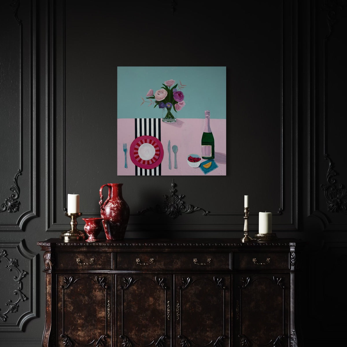 A pastel tabletop setting with a pink striped plate, utensils, a bottle of champagne, a bowl of raspberries, and a bouquet of flowers in a clear vase. Hung in a dining room with a dark wall color.