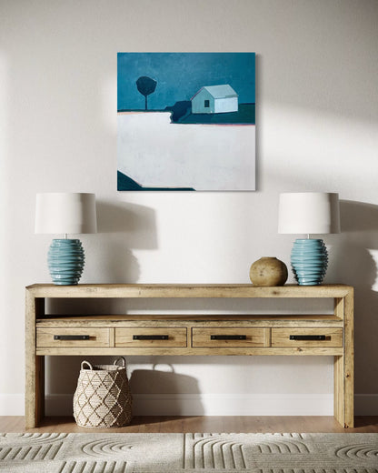 Wooden console table with two lamps and a woven basket, featuring a blue abstract landscape painting above.