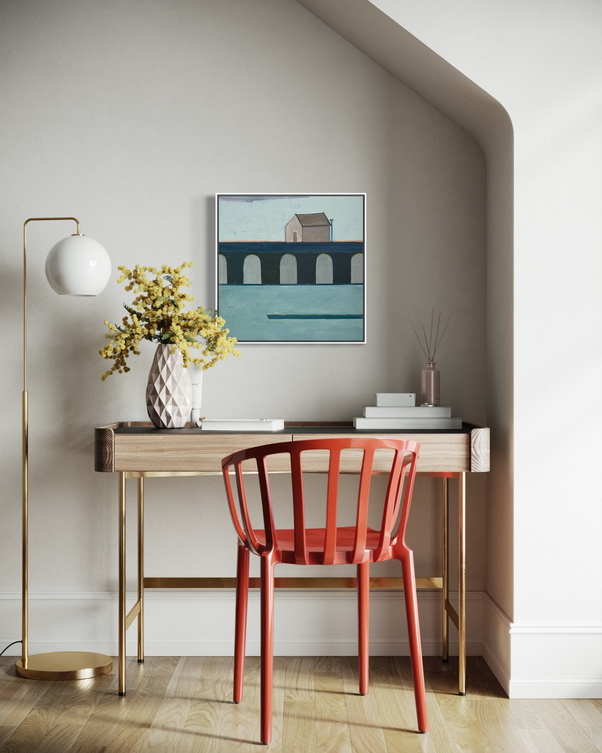 Painting of a house hung over a desk with a vase of flowers.