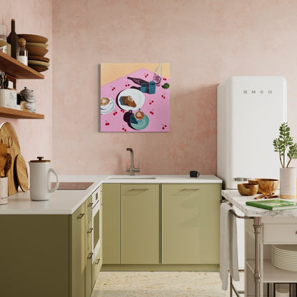 A colorful abstract art painting depicting a breakfast table scene with a croissant on a plate , 2 coffee cups, hanging on a pink kitchen wall above sage green cabinets.