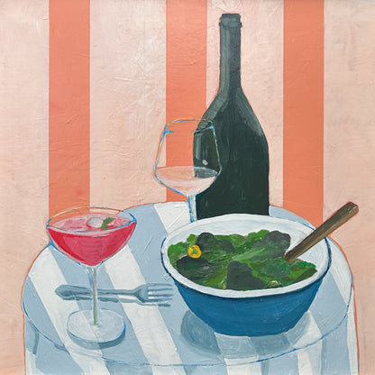 A still life painting of a dining table scene with a blue bowl of green salad, a pink cocktail in a coupe glass, a wine glass, and a dark wine bottle against a pink and white striped background.