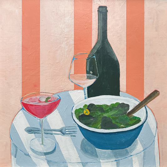 A still life painting of a dining table scene with a blue bowl of green salad, a pink cocktail in a coupe glass, a wine glass, and a dark wine bottle against a pink and white striped background.