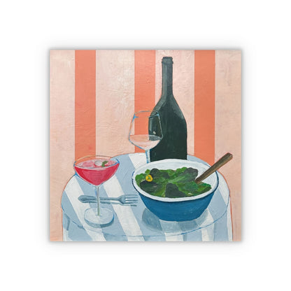 A square painting featuring a still life painting of a table setting with a pink cocktail, a bowl of green salad, a wine glass, and a dark wine bottle against a peach and orange striped background shown as a square on a white background with a drop shadow. 