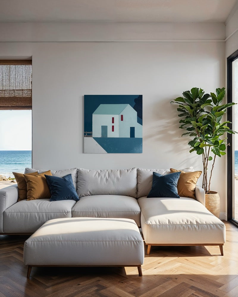 A modern living room scene featuring a light gray sectional sofa with navy and mustard accent pillows, a matching ottoman, a potted fiddle-leaf fig plant, and a geometric house painting on the wall overlooking the ocean.