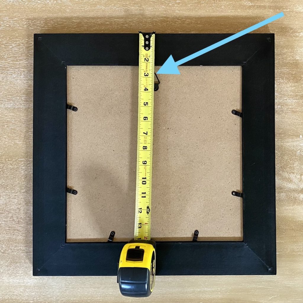 image of the back of a picture frame with tape measure measuring where the picture hanger is
