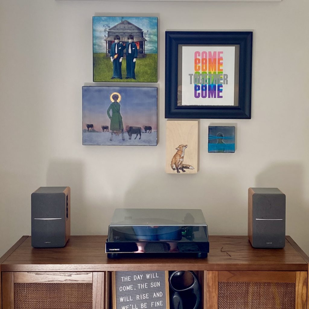 finished image of gallery wall with artwork hung above sideboard that has a record player on top
